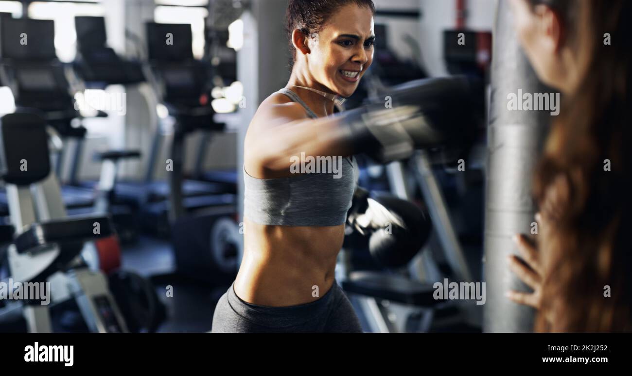 Gib alles, was du hast. Eine kurze Aufnahme einer jungen Boxerin, die mit ihrem Trainer im Fitnessstudio an einem Boxsack trainiert. Stockfoto