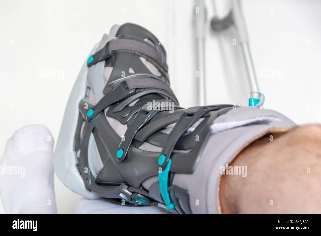 Der europäische Mann nach der Achillessehnenruptur ist wieder zu Hause mit einem speziellen Physiotherapieschuh und Krücken für die Heilung zu Hause mit gesunden Medikamenten Schmerzmittel gegen das schmerzende Bein Stockfoto