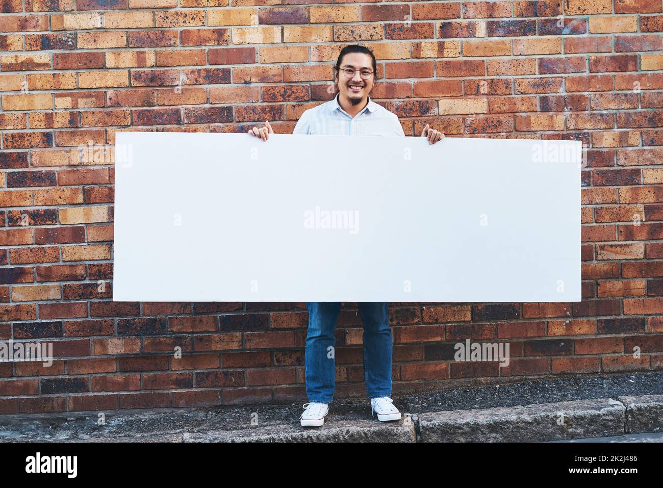 Was würden Sie mit all diesem Raum tun? Aufnahme eines jungen Mannes, der ein leeres Banner vor einem städtischen Hintergrund im Freien hält. Stockfoto