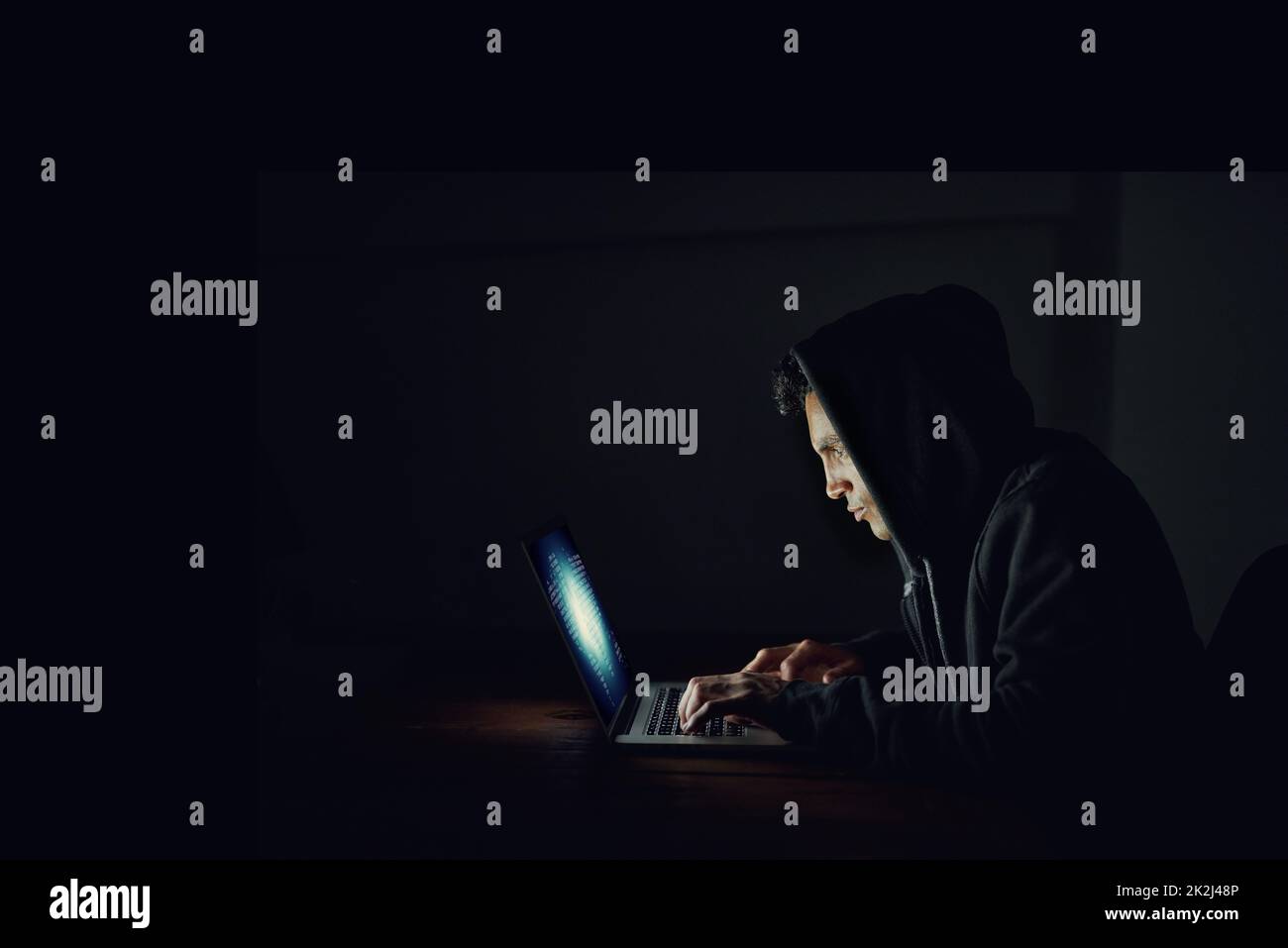Sich selbst bei Ihren Passwörtern helfen. Aufnahme eines verdunkelten Computerhackers mit einem Laptop im Dunkeln. Stockfoto