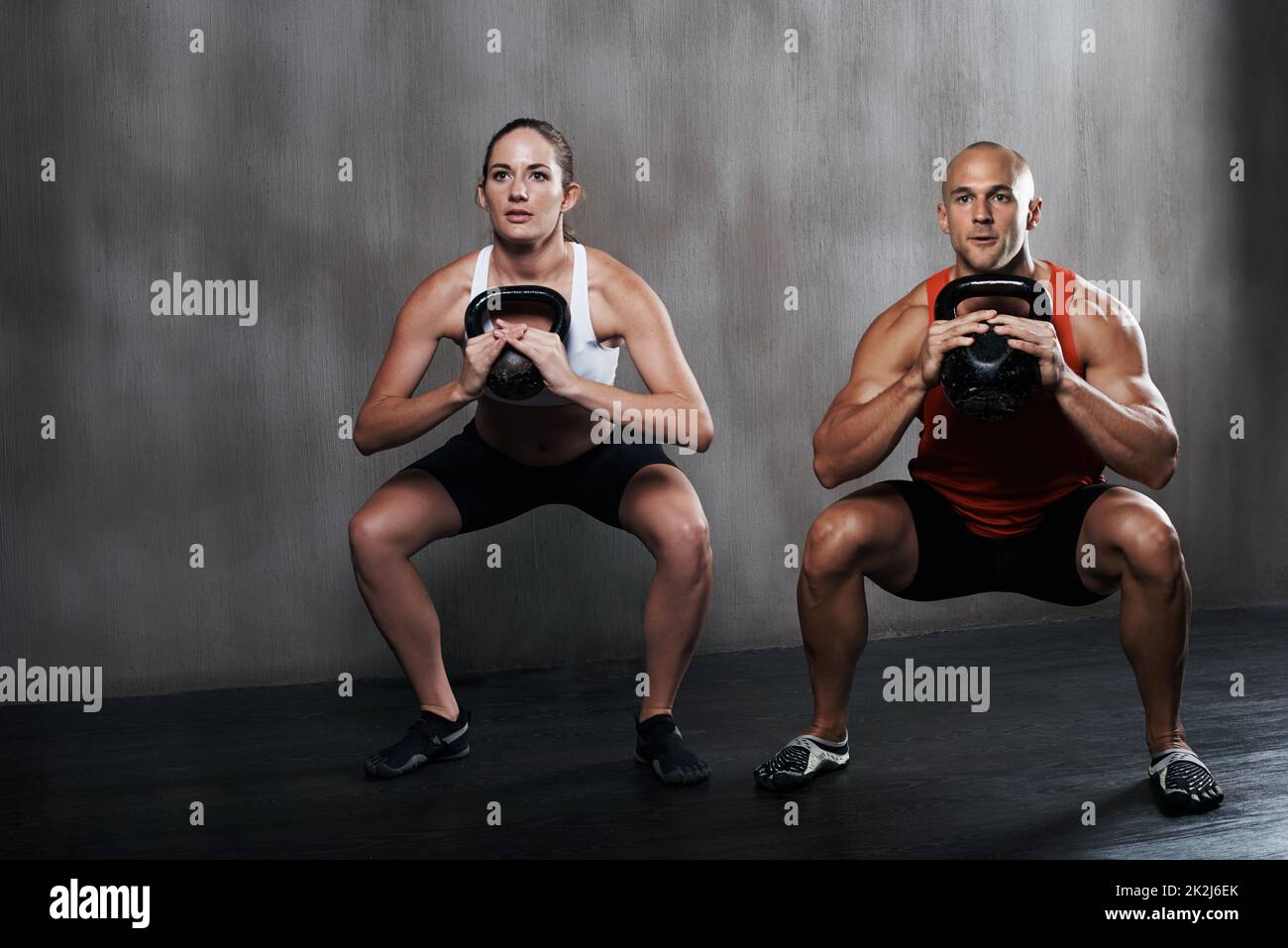 Trainiere verrückt oder bleibe gleich. Ein Mann und eine Frau trainieren mit den Kettelglocken im Fitnessstudio. Stockfoto