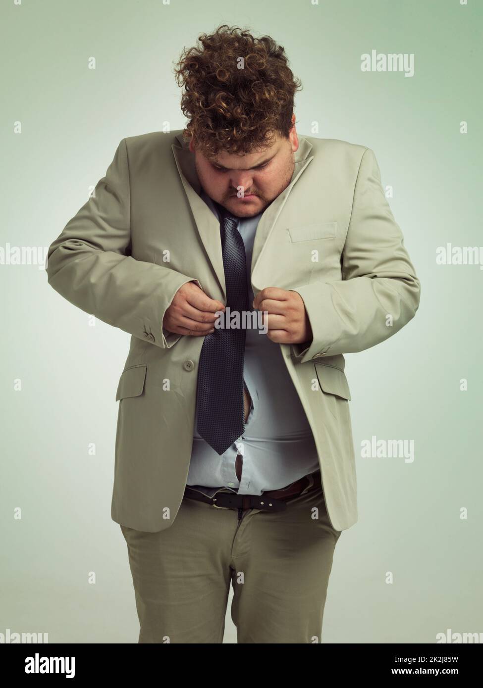 Wie wird das gemacht? Aufnahme eines übergewichtigen Mannes in einem Anzug, der versucht, seine Jacke zu drücken. Stockfoto
