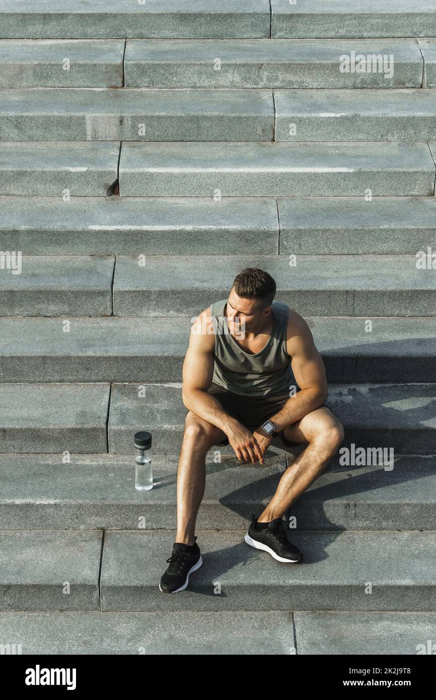 Selbstbewusster, athletischer Mann, der nach dem Fitnesstraining im Freien auf Betontreppen sitzt Stockfoto