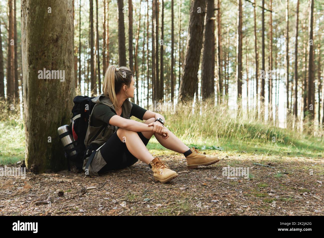 Weibliche Wanderer bei einem kleinen Halt, die auf dem Boden im grünen Wald sitzen Stockfoto