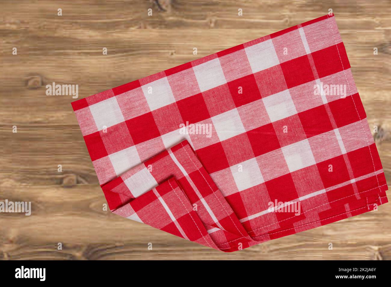 Leeres Tischprodukt. Blick von oben auf einen rustikalen Holztisch mit rot-weiß karierter Tischdecke oder Serviette. Vorlage für die Montage Ihrer Lebensmittel- und Produktpräsentation. Platz für Essensrezepte. Stockfoto