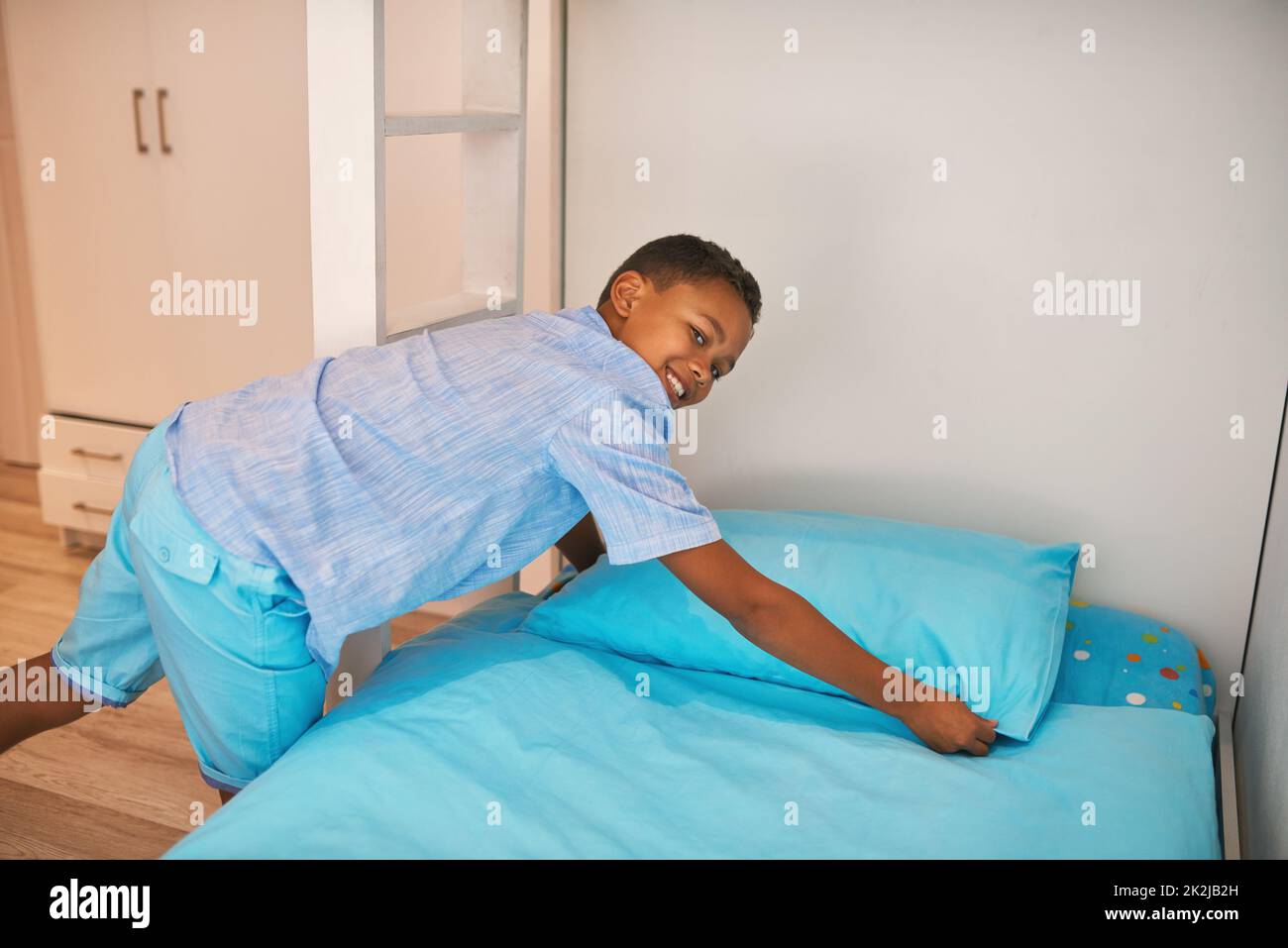 Das Bett wird genammt. Porträt eines jungen Jungen, der ein Bett macht. Stockfoto