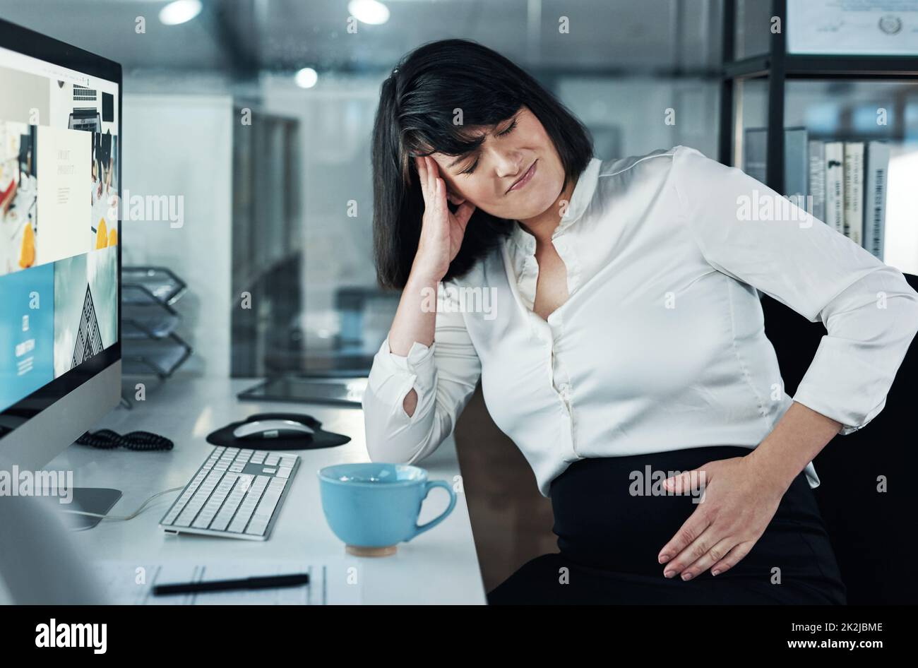 Warum tut das so weh. Kurzer Schuss einer attraktiven, schwanger werdenden Geschäftsfrau, die allein im Büro sitzt und unter Bauchschmerzen leidet. Stockfoto