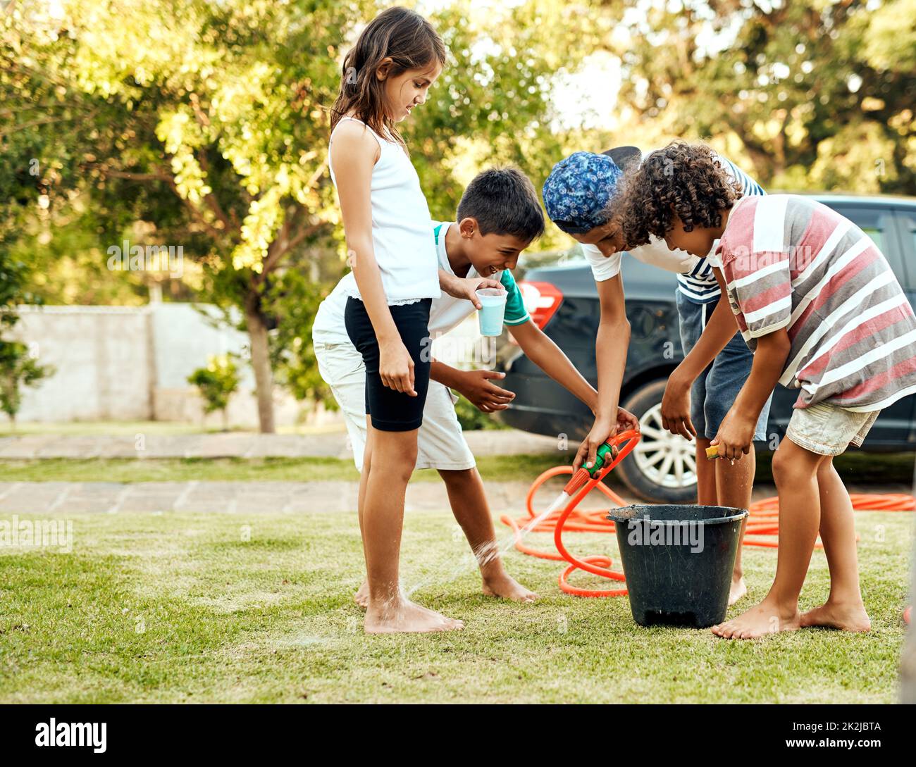 Scheuern Sie den ganzen Abrieb weg. Aufnahme einer Gruppe fröhlicher junger Kinder, die tagsüber draußen ihr Elternauto waschen. Stockfoto