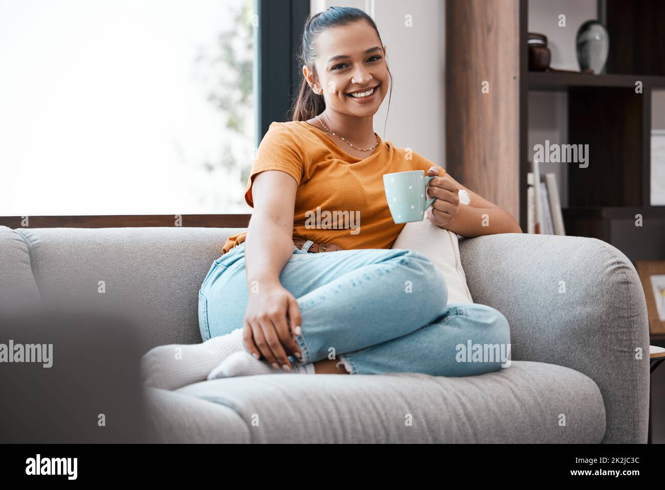 Nichts Besseres als eine warme Tasse Kaffee. Aufnahme einer jungen Frau, die sich zu Hause auf der Couch entspannt. Stockfoto