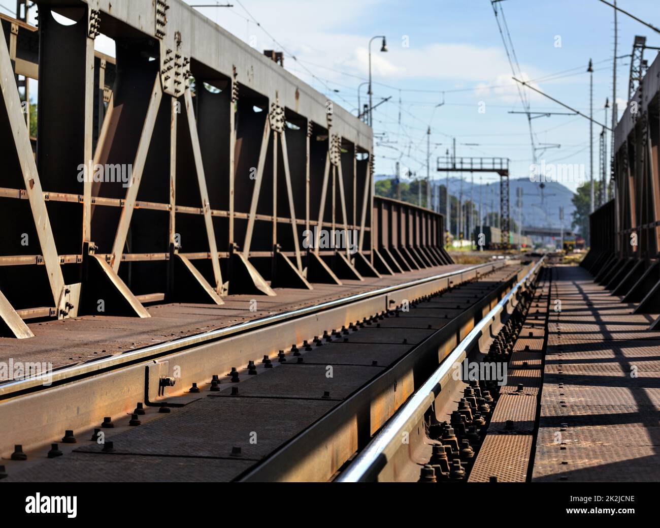 Blick von der alten Eisenbahnbrücke, Braun von Rost, Schienen, Kabel und elektrische Beiträge in Ferne sichtbar. Stockfoto