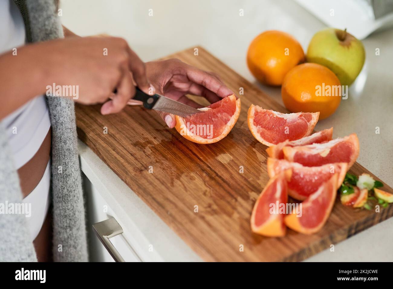 Gesund essen, glücklich sein. Aufnahme einer nicht identifizierbaren Frau, die in ihrer Küche zu Hause Obst zum Frühstück schneidet. Stockfoto