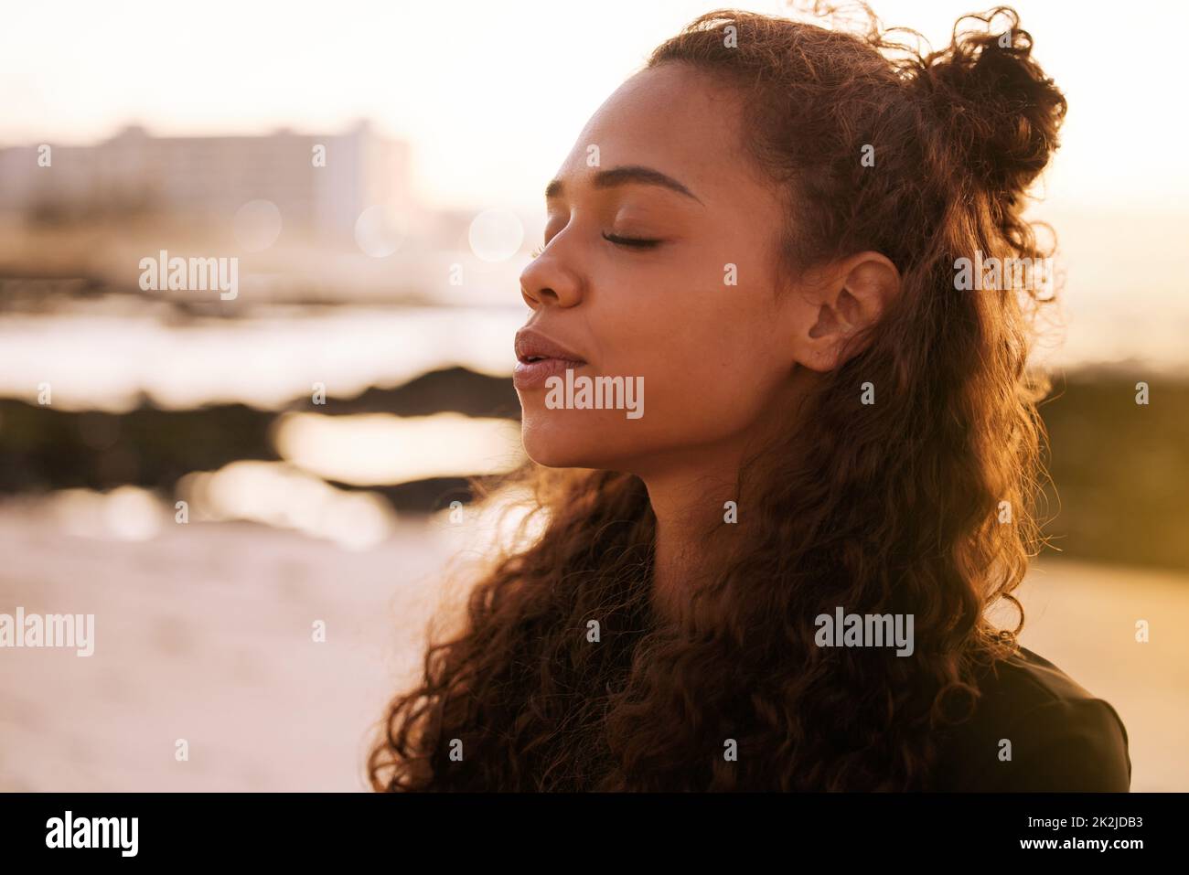 Das Universum spricht, wenn man anhält und zuhört. Aufnahme einer attraktiven jungen Frau, die allein auf einer Matte sitzt und bei Sonnenuntergang am Strand meditiert. Stockfoto