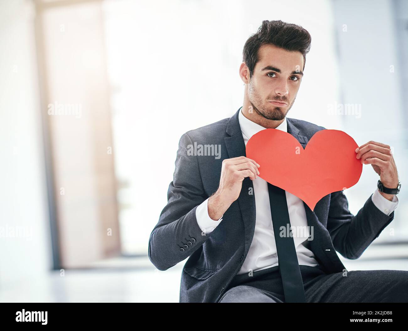 Mir würde ein wenig Büroromantik nichts ausmachen. Porträt eines trendigen jungen Geschäftsmannes, der mit einem Papierherz im Büro posiert. Stockfoto