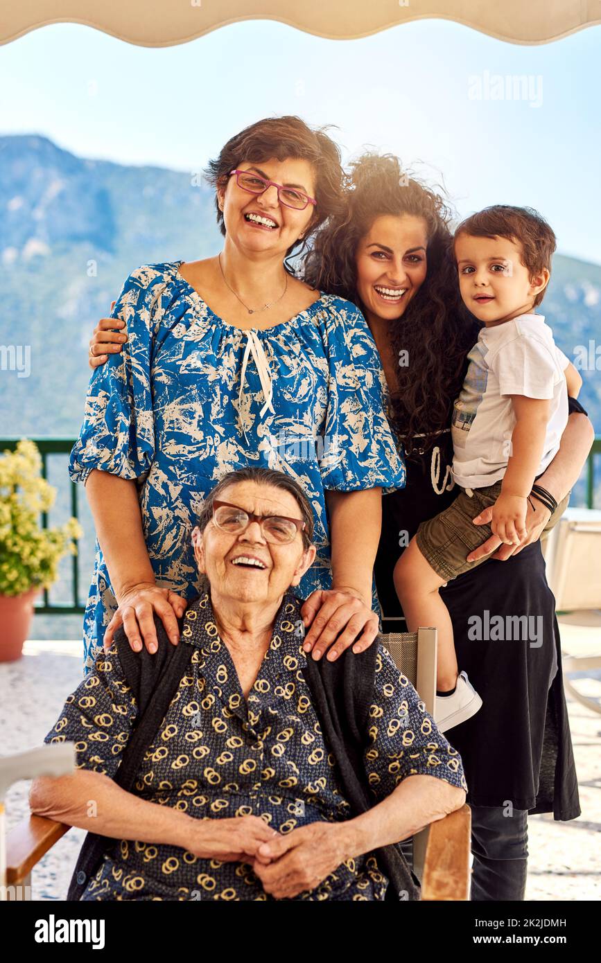Vier Generationen leben zusammen. Porträt einer fröhlichen Familie, die sich gegenseitig hält, während sie draußen zu Hause in die Kamera blickt. Stockfoto