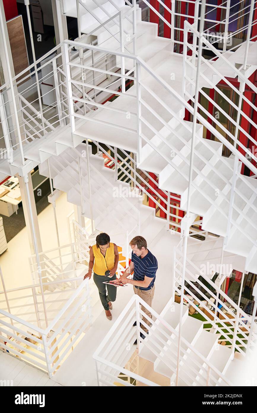 Auf dem Weg an die Spitze aufholen. Aufnahme von zwei Kollegen, die miteinander reden, während sie in einem Büro auf einer Treppe stehen. Stockfoto