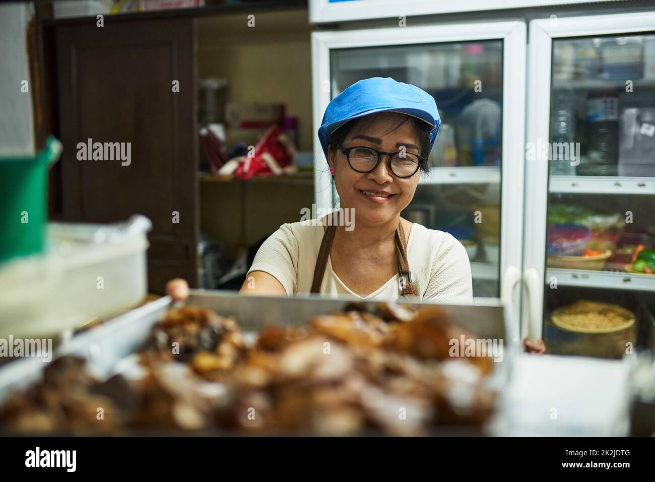 Bestellen. Porträt eines glücklichen Kochs, der ein Tablett mit Speisen in einem thailändischen Restaurant auf den Pass legt. Stockfoto