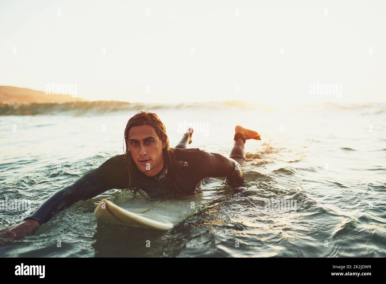 Beim Surfen geht es darum, den Rhythmus des Ozeans zu spüren. Porträt eines jungen Mannes, der auf einem Surfbrett im Meer paddelt. Stockfoto