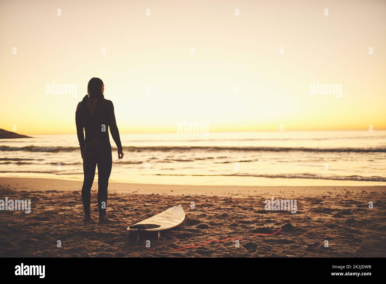 Beim Surfen spüren Sie die Kühle und Ruhe der Natur. Rückansicht eines jungen Surfers, der am Strand auf das Meer blickt. Stockfoto