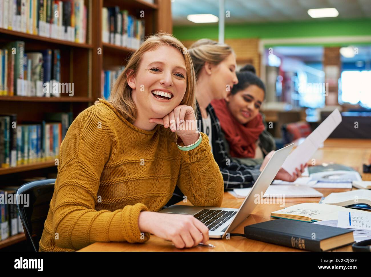 Sie ist sich sicher, dass sie den Test bestehen wird. Porträt einer fröhlichen jungen Studentin, die an ihrem Laptop arbeitet und in einer Bibliothek studiert. Stockfoto