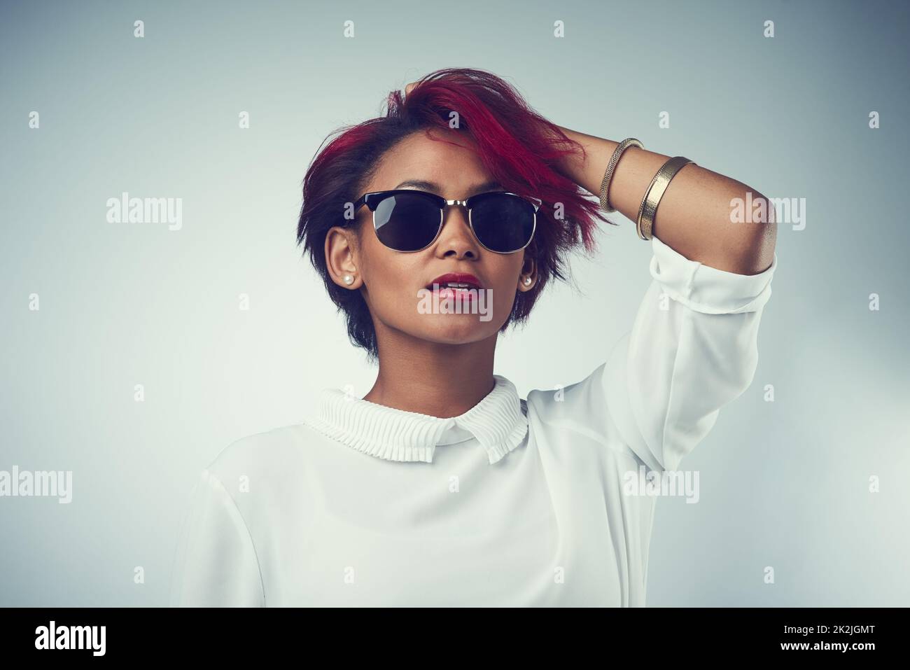 Besitzen Sie einfach Ihre Schönheit. Aufnahme einer schönen jungen Frau, die vor grauem Hintergrund eine Sonnenbrille trägt. Stockfoto