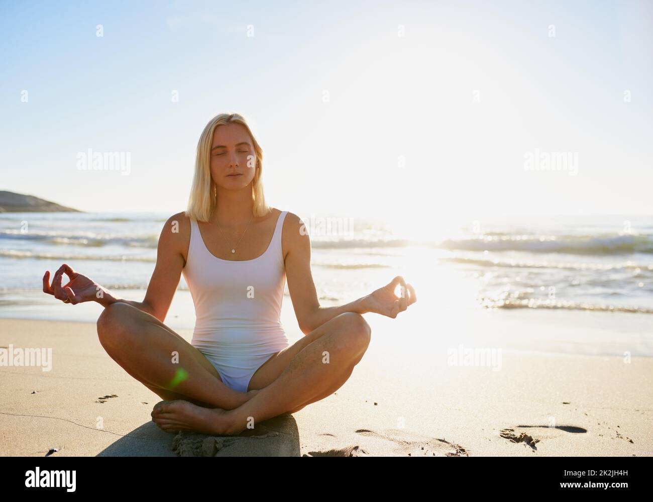 Namaste genau hier. Ganzkörperaufnahme einer attraktiven jungen Frau, die mit gekreuzten Beinen am Strand sitzt und meditiert. Stockfoto