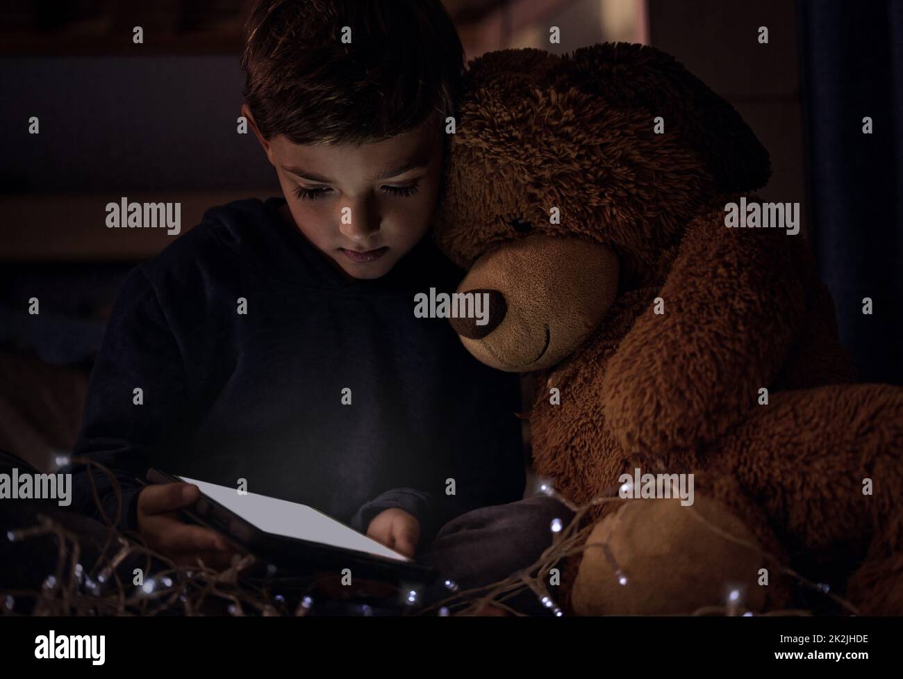 Das Königreich gehört kleinen Kindern. Aufnahme eines entzückenden kleinen Jungen, der nachts in seinem Schlafzimmer ein digitales Tablet mit seinem Teddybären benutzt. Stockfoto