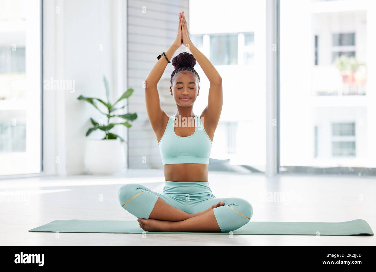 Eins werden mit dem Universum. In voller Länge eine attraktive junge Frau, die allein mit gekreuzten Beinen sitzt und im Studio Yoga praktiziert. Stockfoto