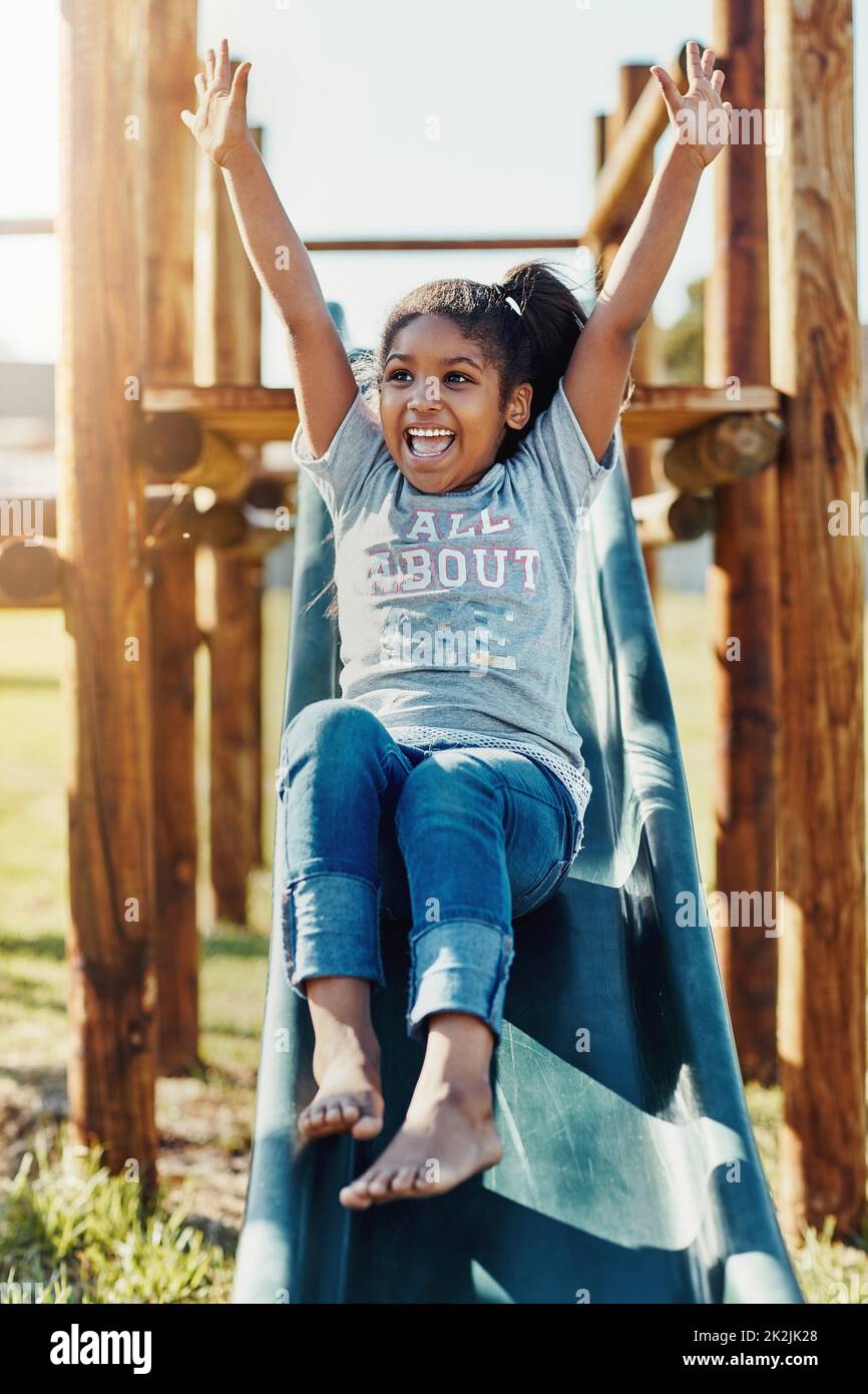Genießen Sie einen Tag voller Spaß. Ganzkörperaufnahme eines entzückenden kleinen Mädchens, das auf einer Rutsche im Park spielt. Stockfoto