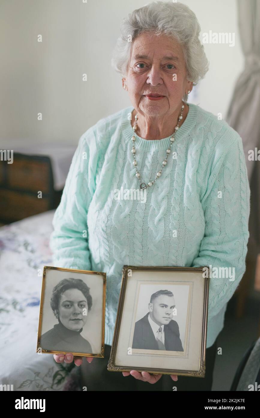 Sie werden immer in Erinnerung bleiben. Porträt einer älteren Frau mit alten Schwarz-Weiß-Fotos eines Mannes und einer Frau. Stockfoto