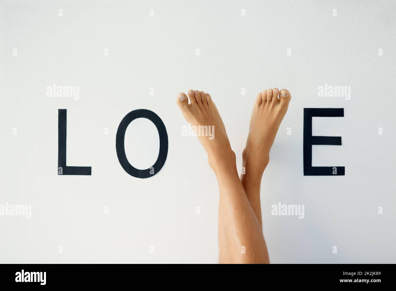 Stehe auf Liebe. Nahaufnahme einer nicht erkennbaren Person, die die Beine kreuzte, wobei seine Füße den Buchstaben V im Wort LIEBE bilden. Stockfoto