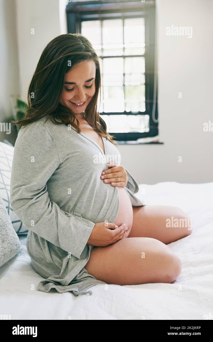 Ich liebe meinen großen Bauch. Aufnahme einer jungen Schwangeren, die sich zu Hause entspannt. Stockfoto