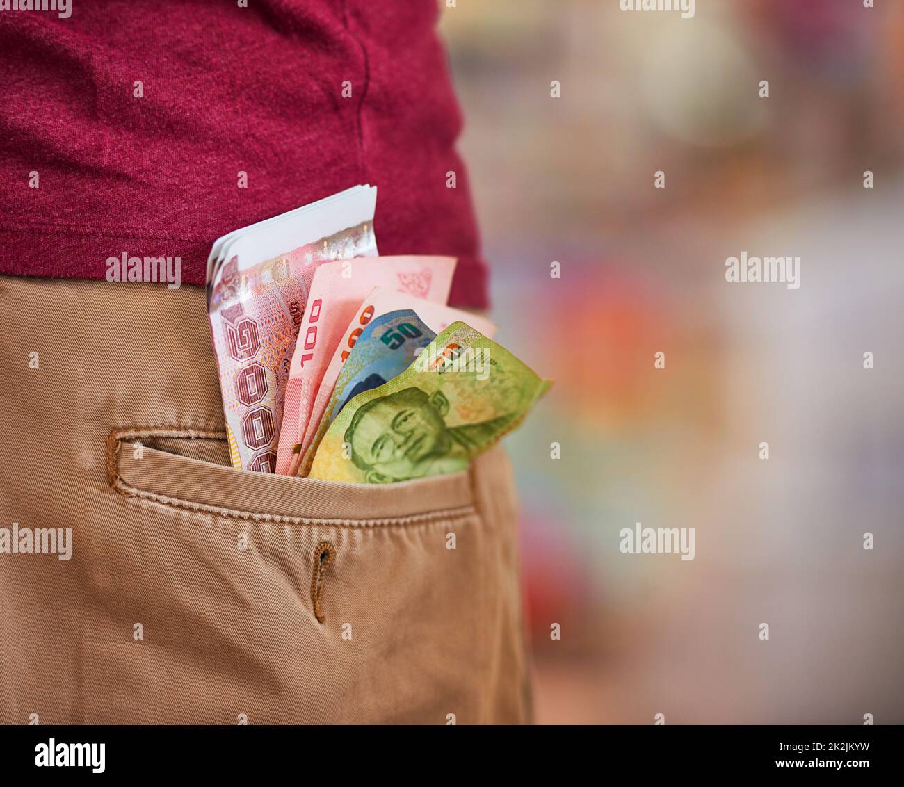 Seien Sie nicht nachlässig mit Ihrem Geld. Kurzer Nahaufnahme eines Mannes mit thailändischem Baht, der aus seiner Gesäßtasche ragt. Stockfoto