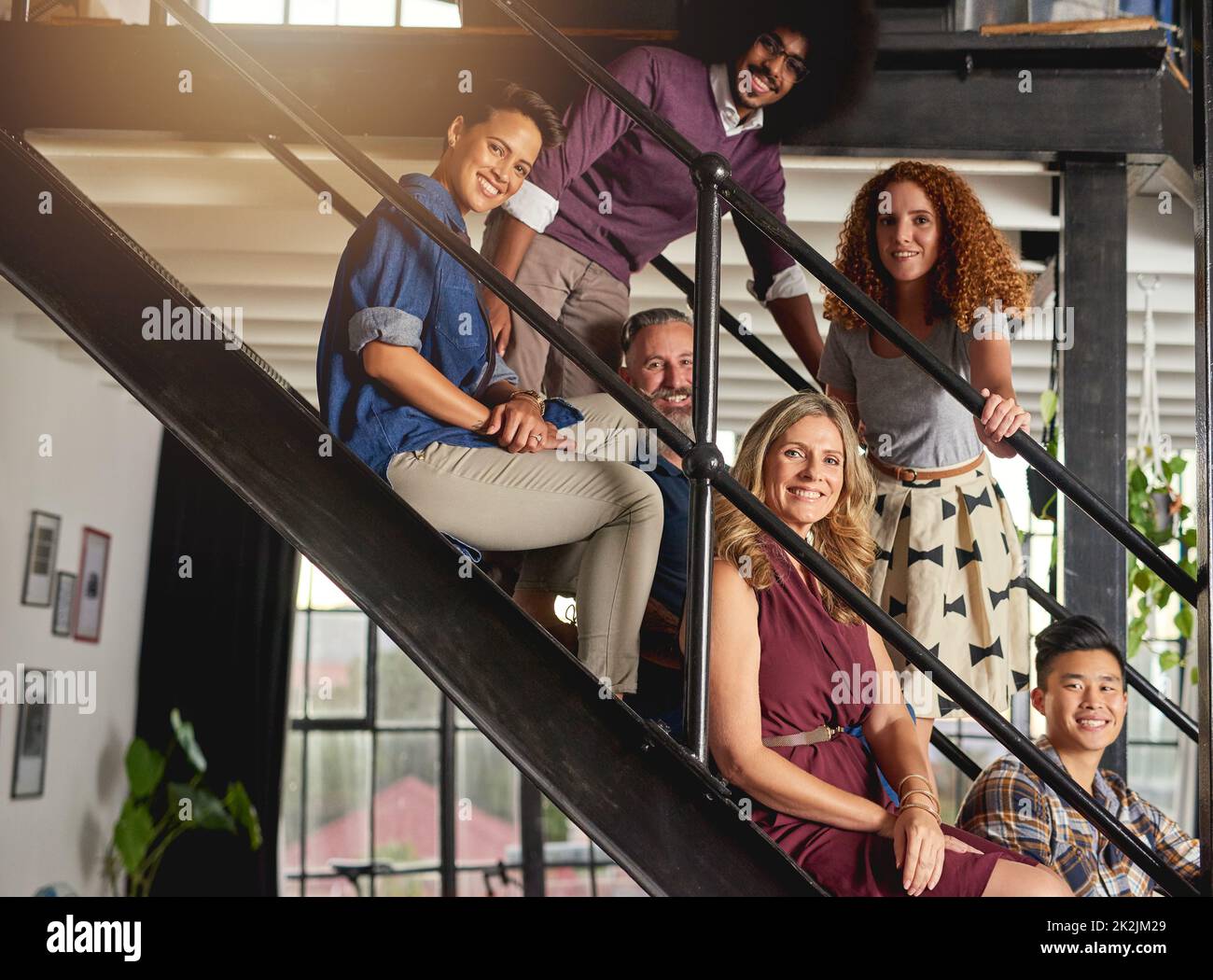 Die Treppe zum kreativen Erfolg ist ein flippiges. Porträt einer Gruppe von kreativen Mitarbeitern, die in einem modernen Büro auf einer Treppe sitzen. Stockfoto