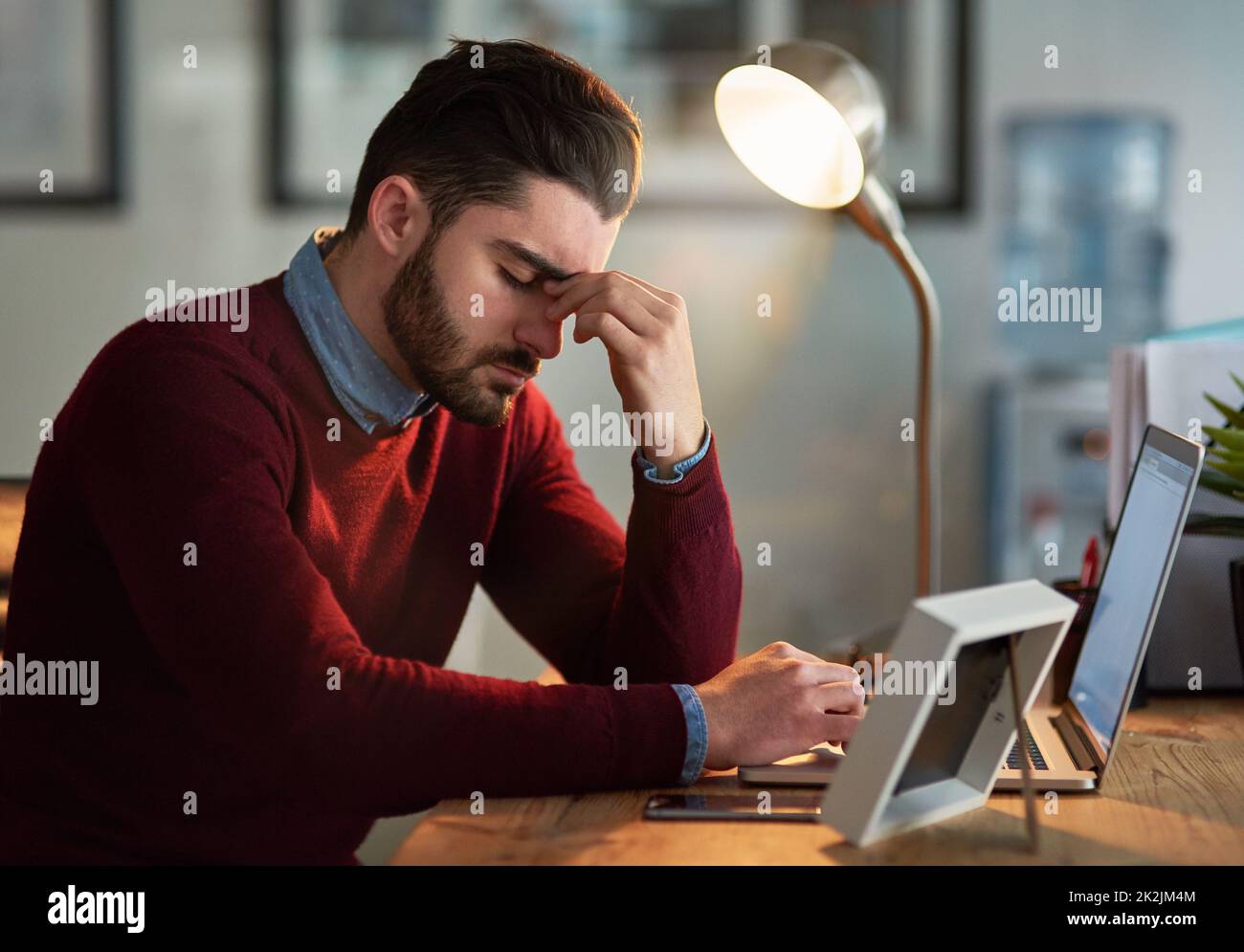 So viel zu tun, so wenig Zeit. Aufnahme eines jungen Designers, der bei seiner Arbeit spät im Büro mit Kopfschmerzen zu kämpfen hat. Stockfoto