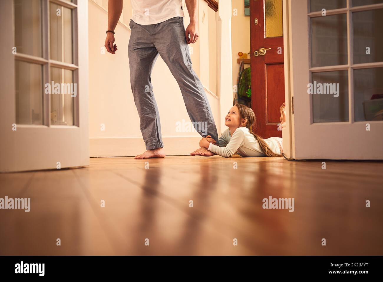 Ich gehe mit dir. Aufnahme eines fröhlichen kleinen Mädchens, das sich am Bein ihres Väter ergriff und nicht losließ, während es zu Hause auf dem Boden lag. Stockfoto