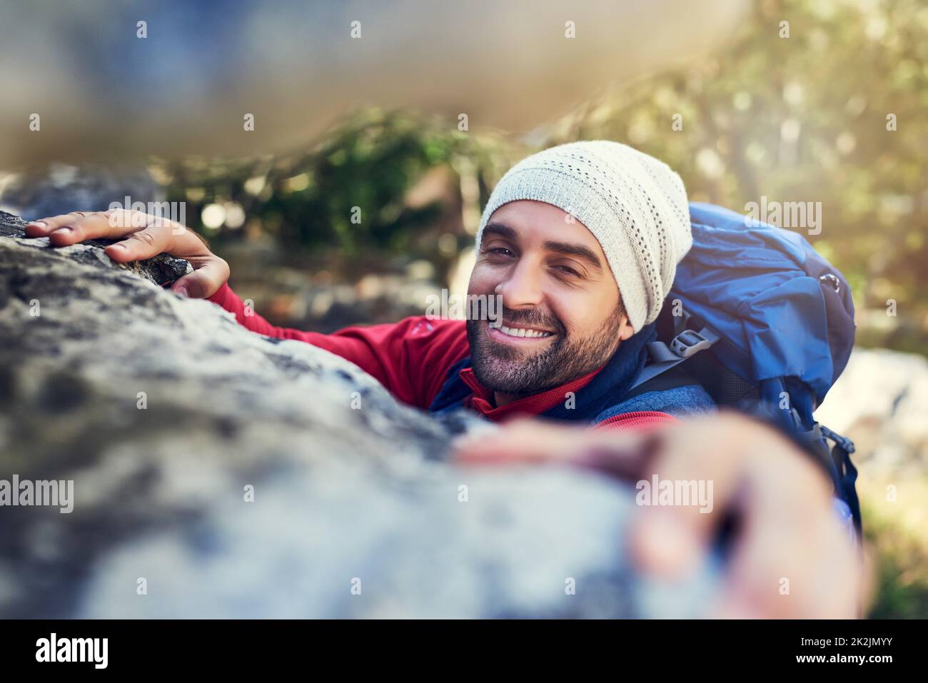 Weiter und nach oben. Porträt eines glücklichen Wanderers, der auf einem Bergpfad über Felsen klettert. Stockfoto