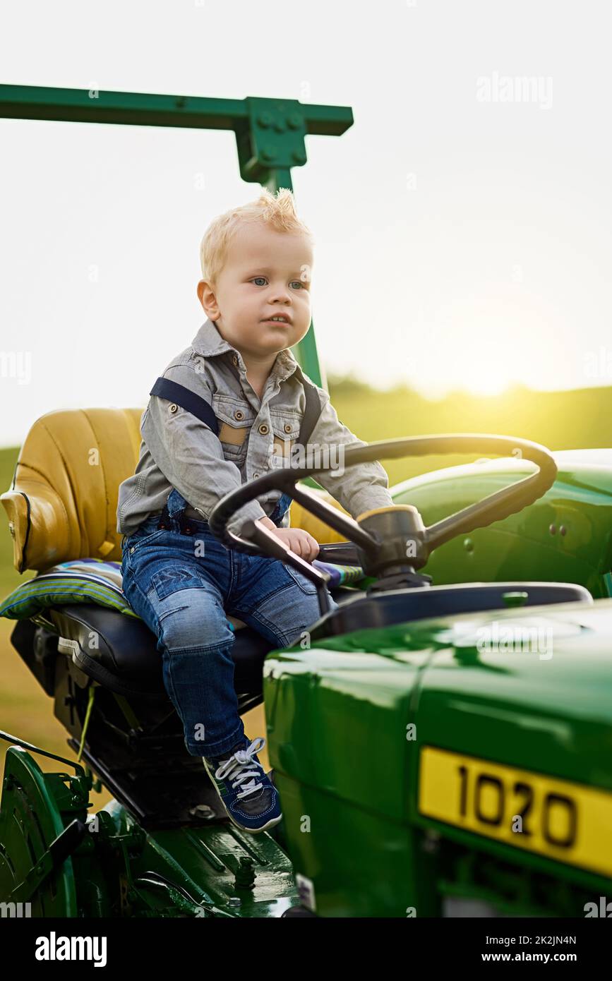 Der kleinste Bauer. Aufnahme eines entzückenden kleinen Jungen, der auf einem Traktor auf einer Farm reitet. Stockfoto