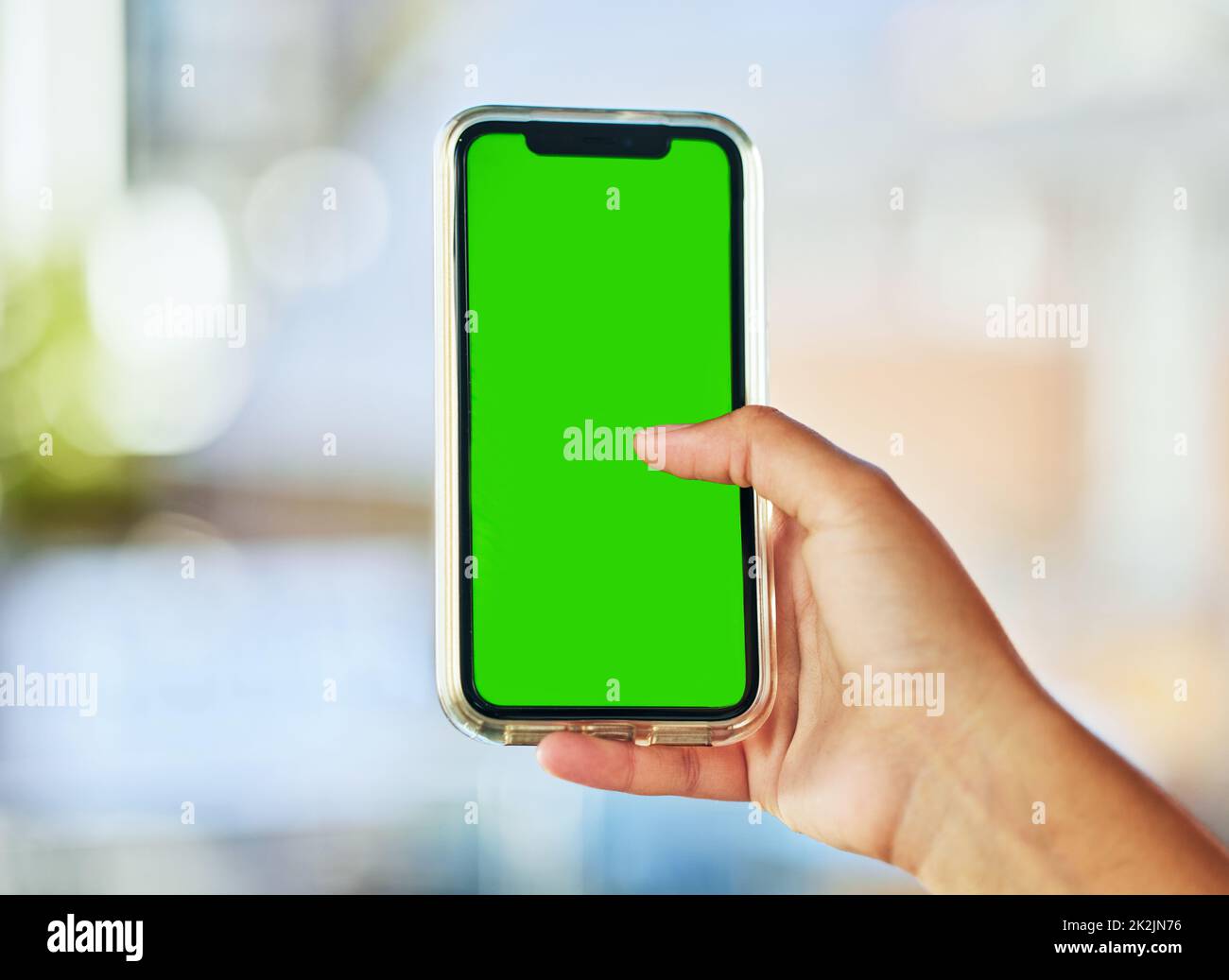 Immer verbunden. Eine junge Frau hält ein Smartphone mit einem grünen Bildschirm vor einem defokussten Hintergrund.. Stockfoto