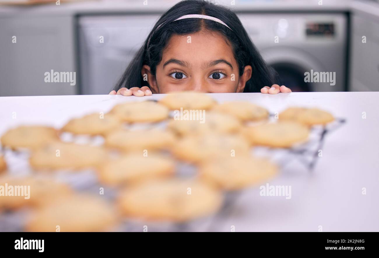 Es ist einfach so verlockend. Aufnahme eines kleinen Mädchens, das über die Küchentheke auf frisch gebackene Plätzchen guckt. Stockfoto