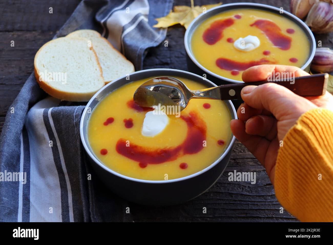 Weiblich in gelb gestrickt Pullover essen Kürbis-Creme-Suppe auf dunklem Holz Hintergrund mit Löffel . Gemütliches Dinner-Konzept im Herbst Stockfoto