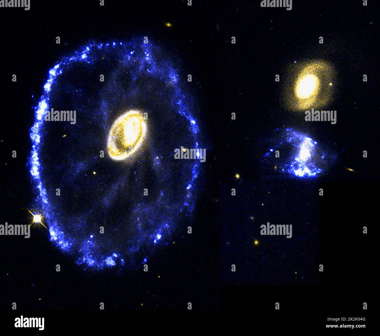 In diesem Hubble-Teleskopbild der Cartwheel-Galaxie, die 500 Millionen Lichtjahre von der Erde entfernt im Sternbild Sculptor liegt, erscheint eine seltene und spektakuläre Kollision zweier Galaxien. Das auffallende ringartige Merkmal ist das direkte Ergebnis einer kleineren Eindringgalaxie – möglicherweise eines von zwei Objekten rechts vom Ring –, die sich durch den Kern [Nahaufnahme unten links] der Wirtsgalaxie abkrümelte. Wie ein in einen See geschleuderter Fels / die Kollision schickte eine Welle von Energie in den Weltraum / pflügte Gas und Staub davor. Stockfoto