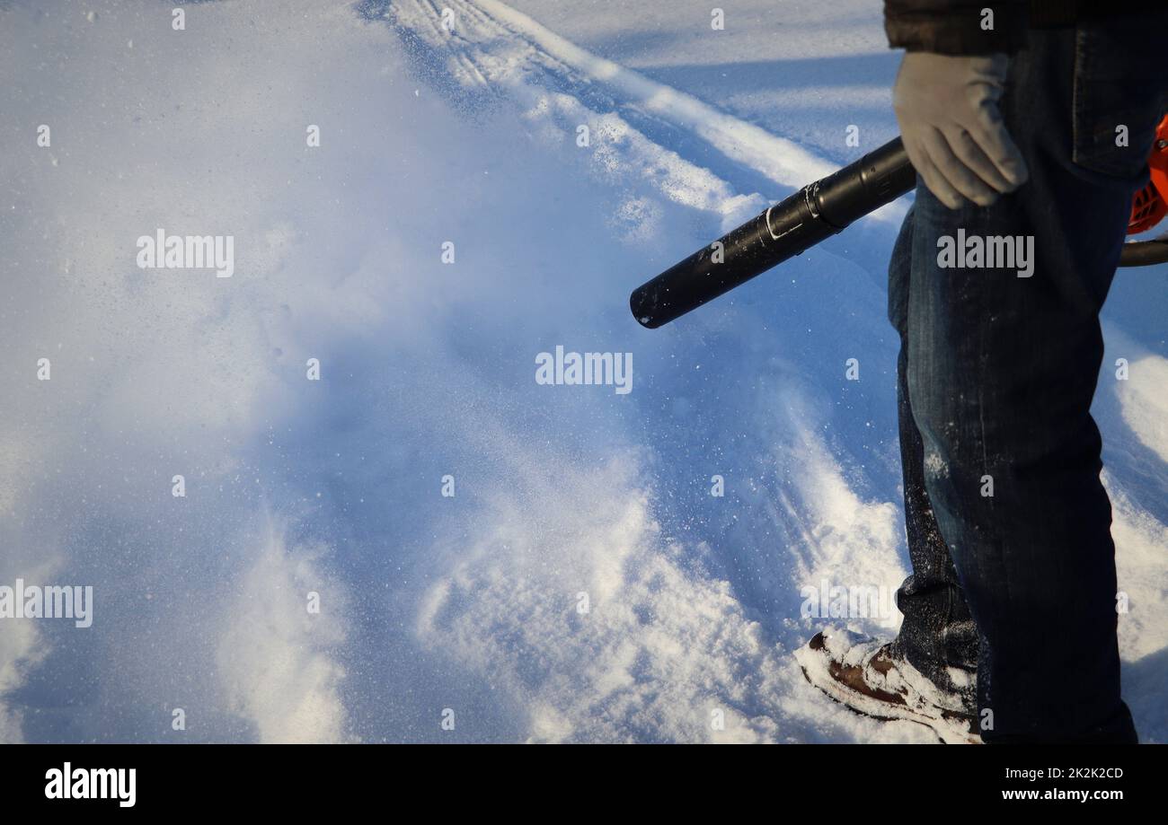 Mann reinigt Bürgersteig von Schnee mit Gebläse Stockfoto