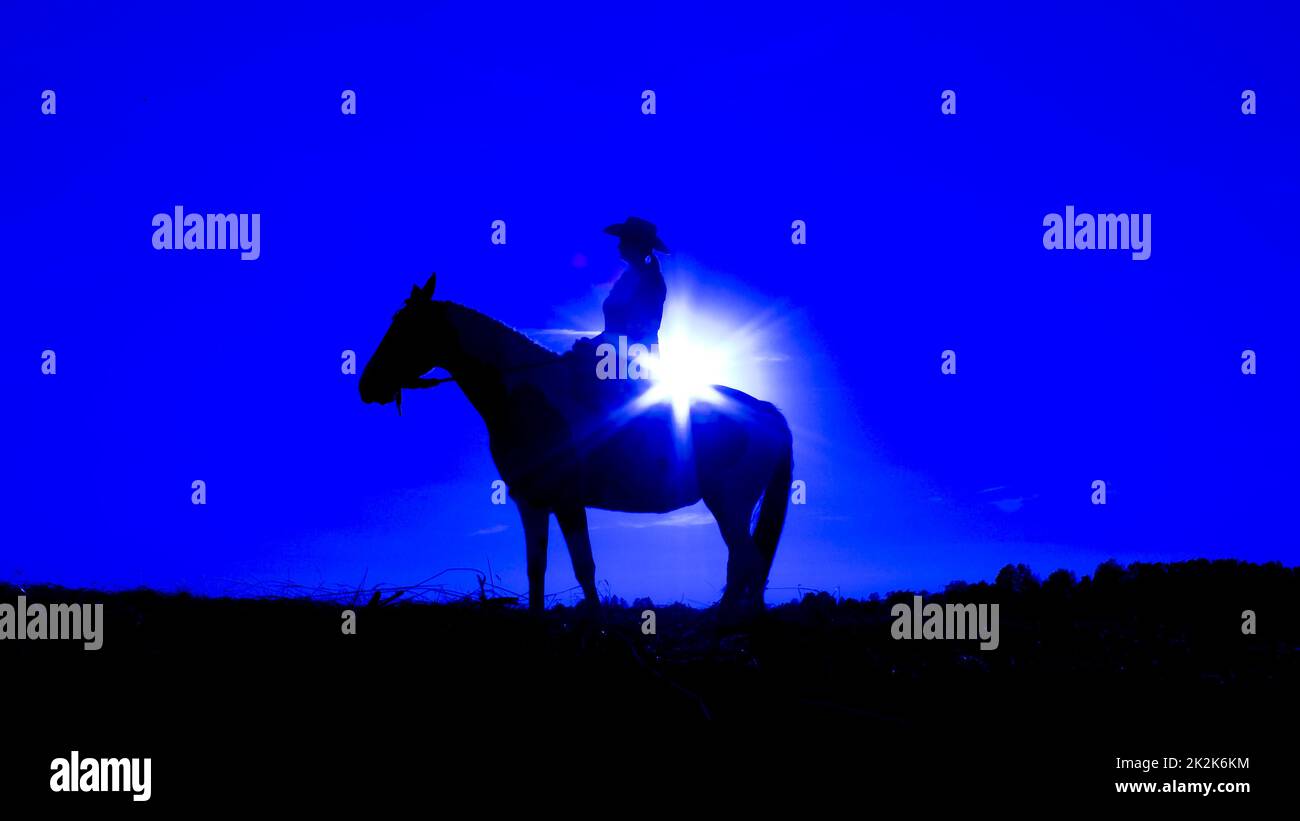 Silhouette Cowgirl auf Pferd bei Sonnenuntergang in Blau Stockfoto
