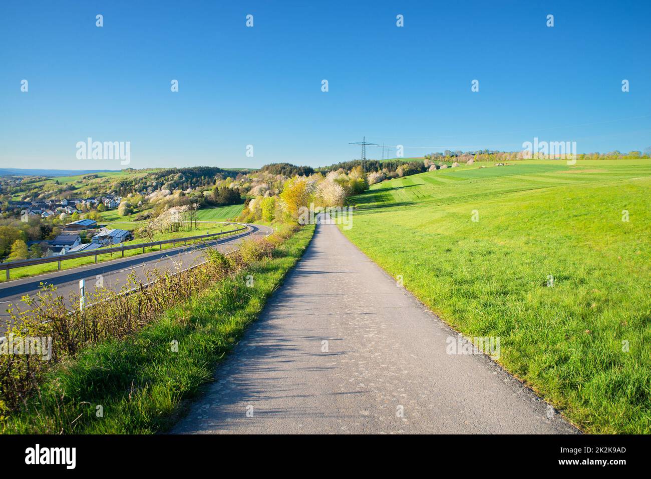 Weg in der Landschaft zwischen einem landwirtschaftlichen Feld und einer Straße, Landschaft in Deutschland, blauer Himmel im Frühling Stockfoto