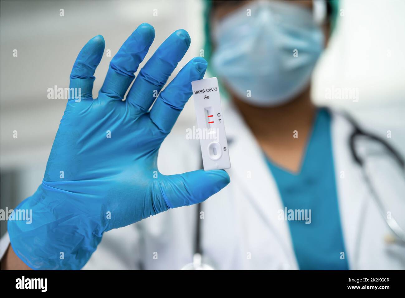 Asiatischer Arzt im PSA-Anzug zeigt ein positives Testergebnis mit Speichel A. Stockfoto