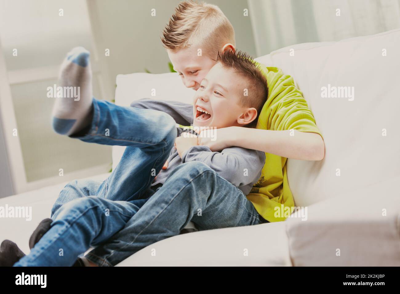 Zwei junge Brüder lachen, während sie auf der Couch rumschnüffeln Stockfoto