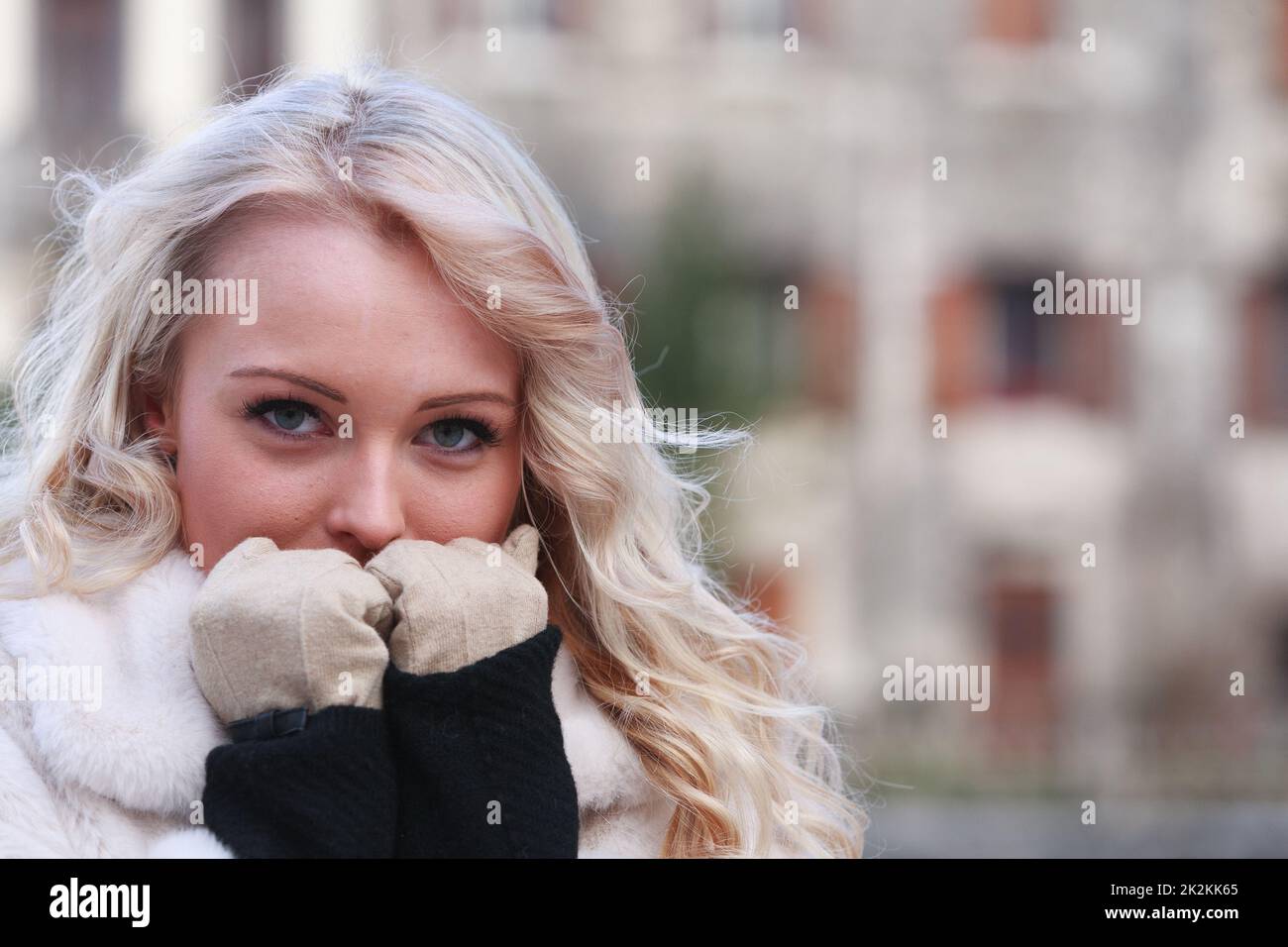 Rücksichtsvolle junge Frau, die ihre mit Handschuhen verkleideten Hände an ihr Gesicht hält Stockfoto