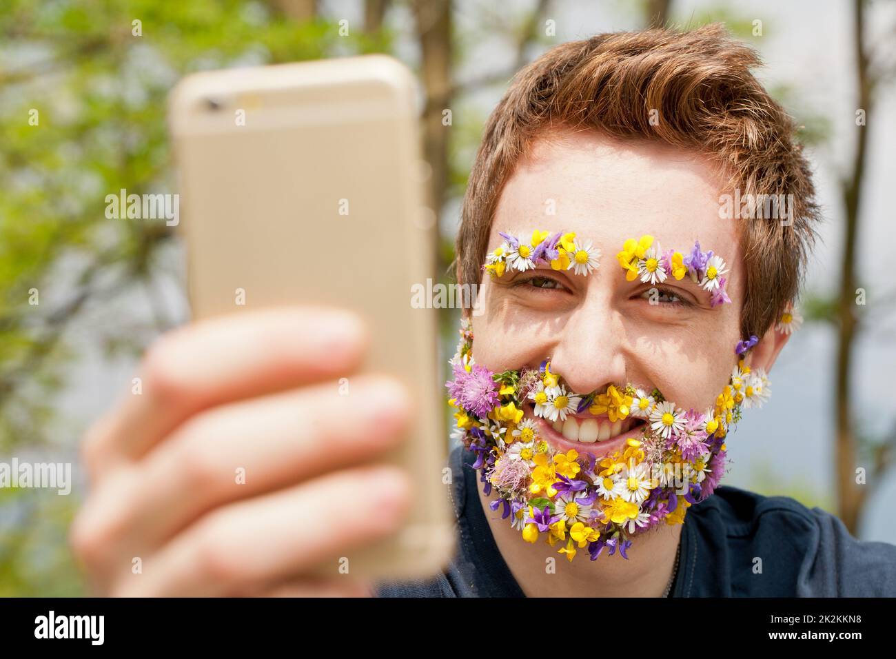 Hipster-Mann mit Blumen bedeckt, der SMS schreibt Stockfoto