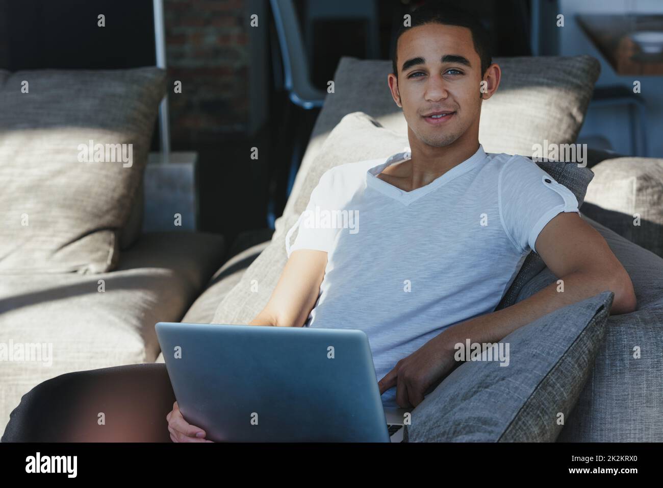 Mann, der sich auf einem bequemen Sofa mit einem Laptop in der warmen Sonne entspannen kann Stockfoto