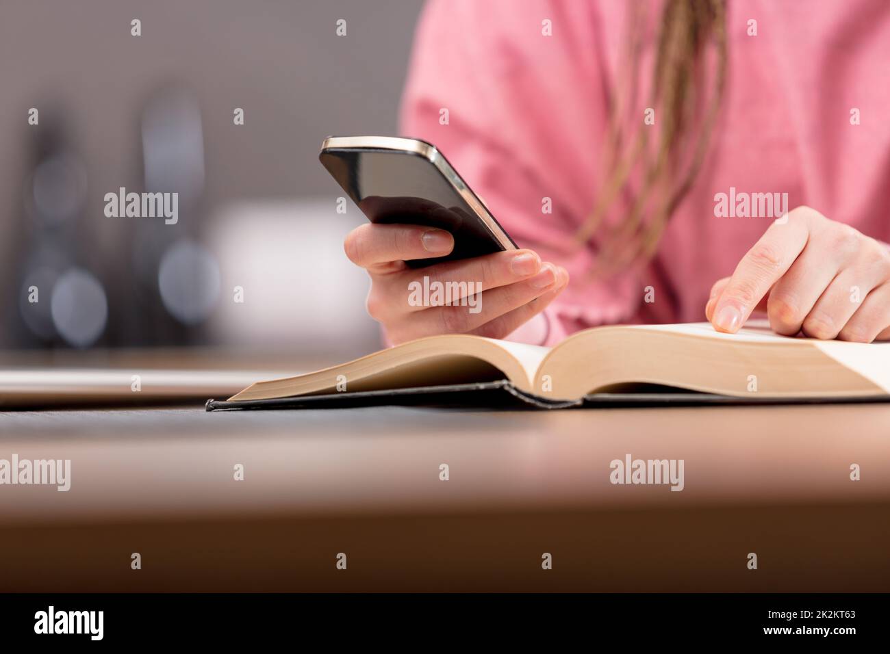 Frau, die beim Lesen eines Buches ein Mobiltelefon benutzt Stockfoto